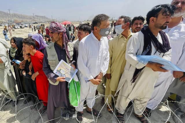 A man holds a certificate acknowledging his work for Americans as hundreds of people gather outside the international airport in Kabul, Afghanistan.