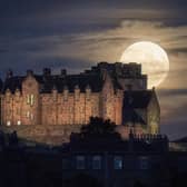 A full moon rises behind Edinburgh Castle on July 23, 2021