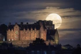 A full moon rises behind Edinburgh Castle on July 23, 2021