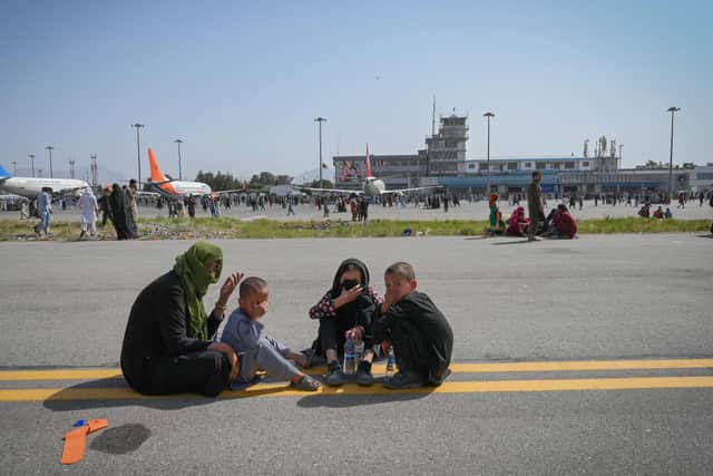 Afghan people sit along the tarmac as they wait to leave the Kabul airport in Kabul on August 16, 2021, after a stunningly swift end to Afghanistan's 20-year war, as thousands of people mobbed the city's airport trying to flee the group's feared hardline brand of Islamist rule. (Photo by Wakil Kohsar / AFP) (Photo by WAKIL KOHSAR/AFP via Getty Images).