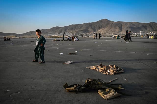 An Afghan child walks near military uniforms as he with elders wait to leave the Kabul airport in Kabul on August 16, 2021, after a stunningly swift end to Afghanistan's 20-year war, as thousands of people mobbed the city's airport trying to flee the group's feared hardline brand of Islamist rule. (Photo by Wakil Kohsar / AFP) (Photo by WAKIL KOHSAR/AFP via Getty Images).