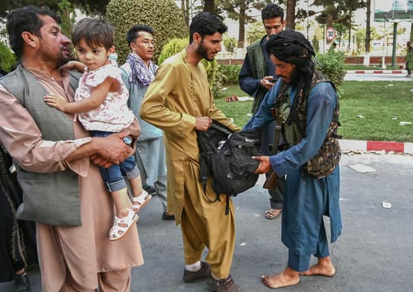 A Taliban fighter (R) searches the bags of people coming out of the Kabul airport in Kabul on August 16, 2021, after a stunningly swift end to Afghanistan's 20-year war, as thousands of people mobbed the city's airport trying to flee the group's feared hardline brand of Islamist rule. (Photo by Wakil Kohsar / AFP) (Photo by WAKIL KOHSAR/AFP via Getty Images).