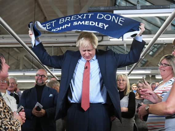 Prime Minister Boris Johnson holds up a banner with the words 'Get Brexit Done' during a visit to the John Smedley Mill, while election campaigning in Matlock, Derbyshire in December 2019. Picture: Stefan Rousseau/PA Wire