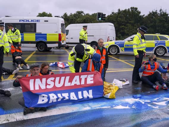 Police officers detain a protester from Insulate Britain occupying a roundabout leading from the M25 motorway to Heathrow Airport in London