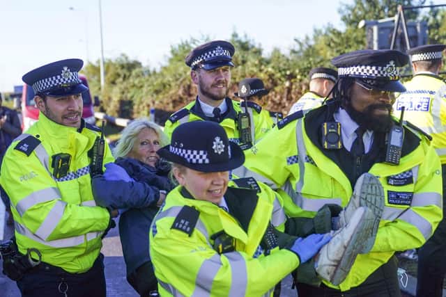 Police officers detain a protester from Insulate Britain occupying a roundabout leading from the M25 motorway to Heathrow Airport in London.