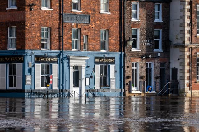 Picture James Hardisty. A person from Lil's Bar & Bistro, clears debris from their flood barrier whilst only a few inches away rising flood water from the River Ouse, floods businesses and properties along King's Staith.
