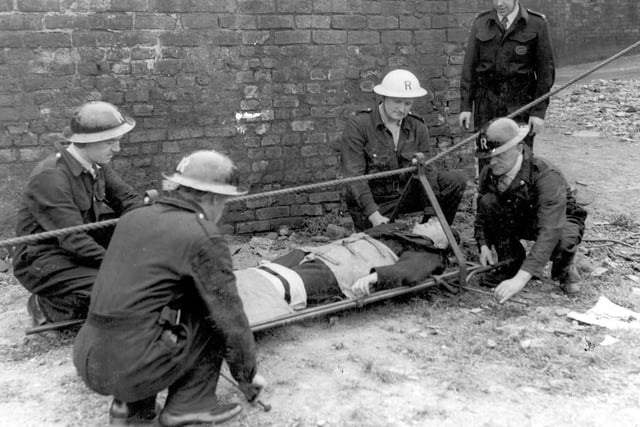 ARP and Rescue services practice the use of stretcher life-line equipment in September 1941. The stretcher has reached the ground with 'casualty'. Men are removing the stretcher form the line.