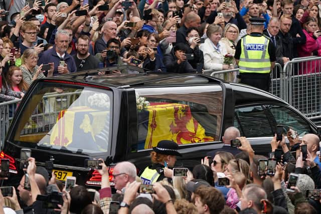 Crowds watch as the hearse carrying the coffin of Queen Elizabeth II, draped with the Royal Standard of Scotland, passes Mercat Cross in Edinburgh, as it continues its journey to the Palace of Holyroodhouse from Balmoral. Picture date: Sunday September 11, 2022.