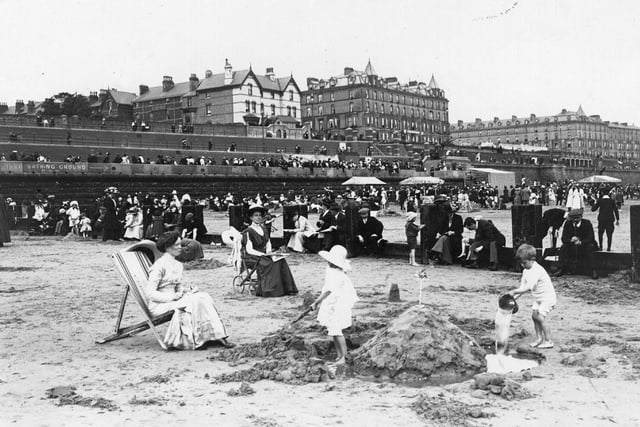 Children building a sandcastle on the beach at Bridlington, which is busy with people.