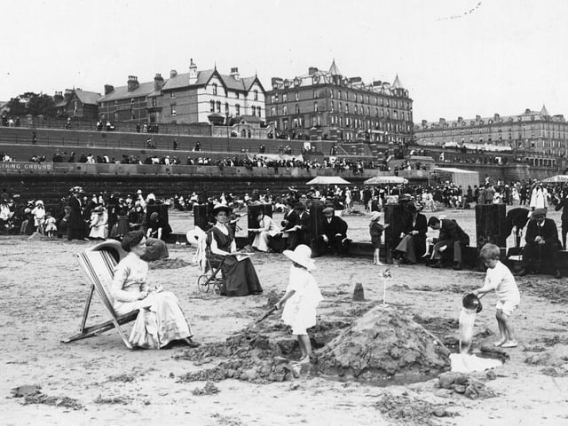 Children building a sandcastle on the beach at Bridlington, which is busy with people.
