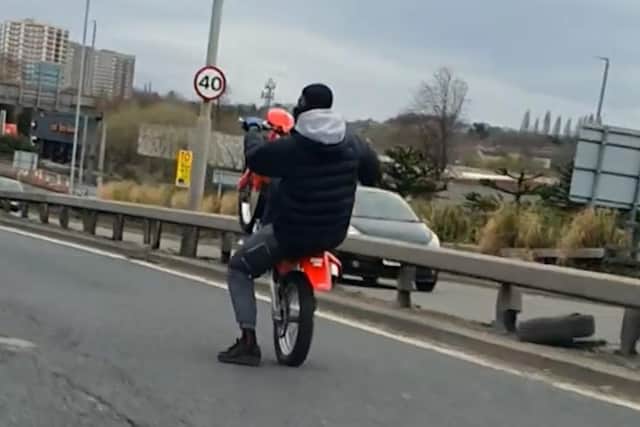 A shocking clip shows the balaclava-clad rider first taunting officers before raising the front wheel of his dirt bike high above his head as he motors alongside them.