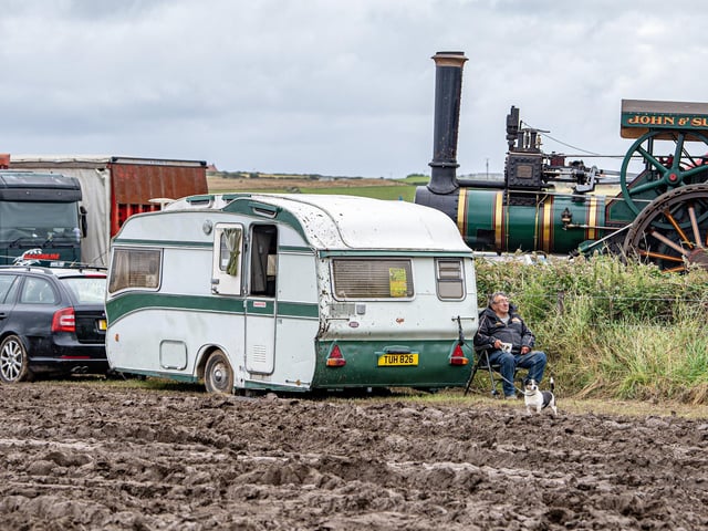 An exhibitor takes a break by his caravan in the mud