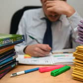 A school teacher looking stressed next to piles of classroom books.
