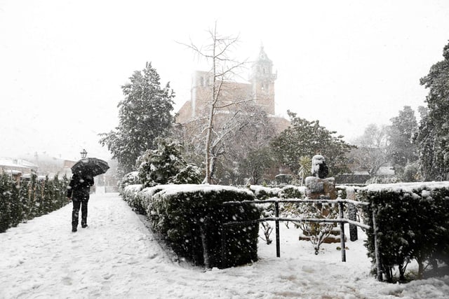 A person walks close to the Cartoixa de Valdemossa palace in the mountain village of Valldemossa covered in snow on the Spanish Balearic island of Mallorca, on February 27, 2023 (Photo by JAIME REINA/AFP via Getty Images)
