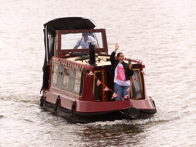 A participant waves from a decorated narrowboat as the flotilla makes its way through Goole during the commemorative voyage