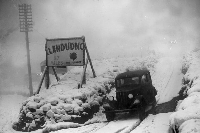 Alongside the snowbound and hazardous Standedge Road in Yorkshire is a well-located advertisement for the Welsh 'sunspot' of Llandudno in December 1937.