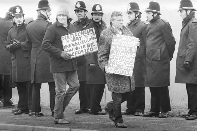 Police patrol the picket line during the Miners' Strike while a miner holds a placard with the legend 'Bentley NUM say the workers united will never be defeated' at the Bentley colliery in Yorkshire, March 20 1984. (Photo by Moore and Nicol/Express Newspapers/Getty Images)