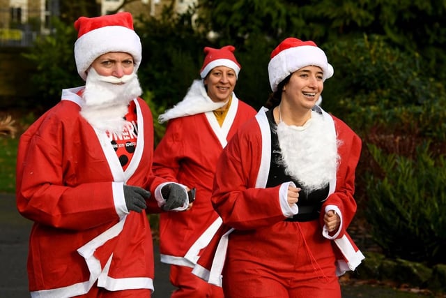 Three people dressed as santas run through the park.