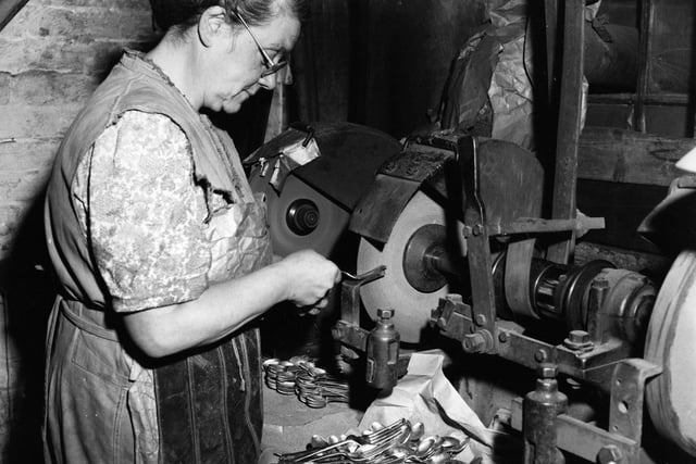 An employee at a factory in Sheffield finishes the prongs of a fork, already roughly cut by machinery, by grinding them on a thin wheel.