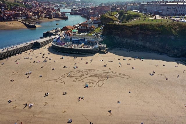 People sunbathe and walk along Whitby beach next to a giant sand drawing of a 50-metre humpback whale. This beach currently has a rating of four and a half stars on TripAdvisor with 1,494 reviews.