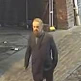 The man in the CCTV image is described as white with a large beard, short possibly greying hair, and he was dressed in a long dark coat with a scarf, lighter trousers, and dark shoes.