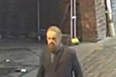 The man in the CCTV image is described as white with a large beard, short possibly greying hair, and he was dressed in a long dark coat with a scarf, lighter trousers, and dark shoes.