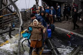 A man helps a woman evacuee cross a destroyed bridge as she and others flee the city of Irpin, northwest of Kyiv, on March 7, 2022. Photo by DIMITAR DILKOFF/AFP via Getty Images.