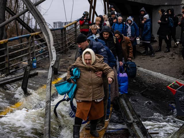 A man helps a woman evacuee cross a destroyed bridge as she and others flee the city of Irpin, northwest of Kyiv, on March 7, 2022. Photo by DIMITAR DILKOFF/AFP via Getty Images.