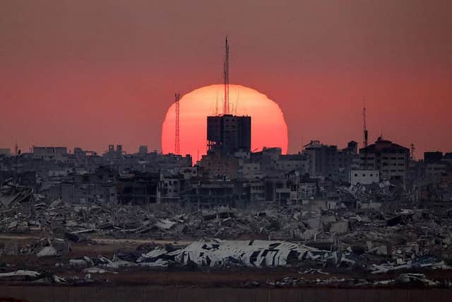 This picture taken from a position on the Israeli border with the Gaza Strip, shows the sun setting behind destroyed buildings in the Palestinian territory, on July 1, 2025. (Photo by Jack GUEZ / AFP via Getty Images).