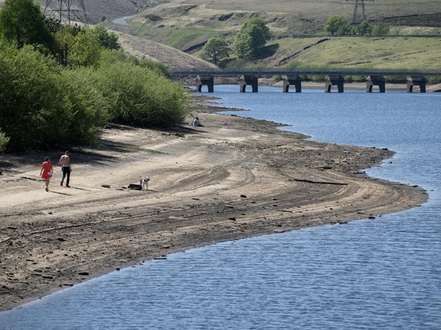 People walk their dog on banks of Baitings Reservoir, which have been partially revealed by a falling water level, near Ripponden. (Photo by Oli SCARFF / AFP) (Photo by OLI SCARFF/AFP via Getty Images)