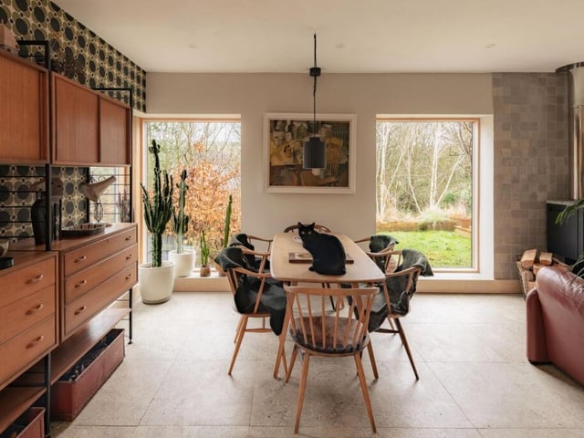 A glass front door opens into a spacious living and dining area, where windows on three sides draw in natural light and frames leafy garden views.