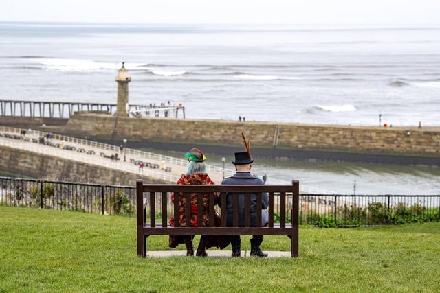 A couple dressed up for Whitby Steampunk Weekend are pictured sitting on a bench overlooking the beach.