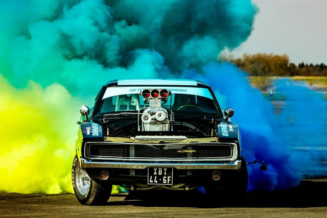 Racing driver Maxfordmosa drives a 1968 Dodge Charger powered by a 10.8L engine reaching over 1600 HP run with E85 Race Fuel whilst he demonstrates his coloured 'Burnout' watched by visitors to the event.