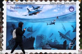 A pedestrian walks past an artwork by the Chesno movement designed as a stamp depicting Russian warships sunk after Ukrainian attacks and Russian President Vladimir Putin drowning in the Black Sea, in the center of Kyiv, on March 15, 2024, amid the Russian invasion in Ukraine. (Photo by Anatolii STEPANOV / AFP)