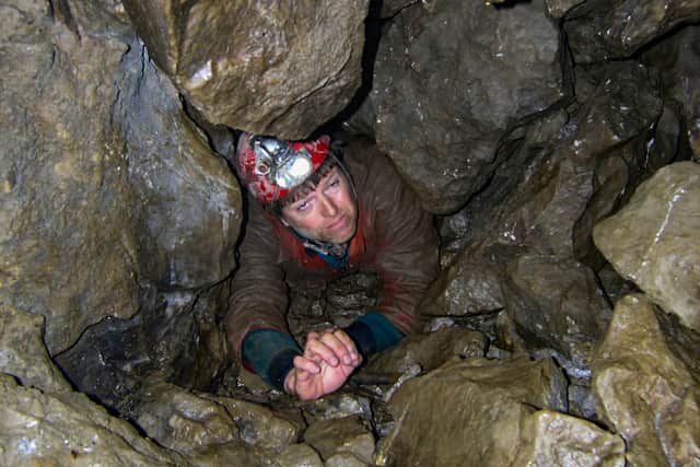 A caver crawls through the final boulder choke of Newby Moss cave, one of many in the Yorkshire Dales. Photo Dave Williams
