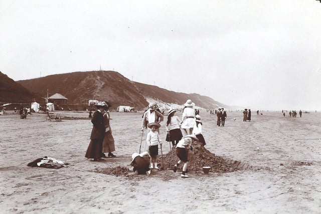 A beach scene at Saltburn showing a family gathered around a sandcastle.