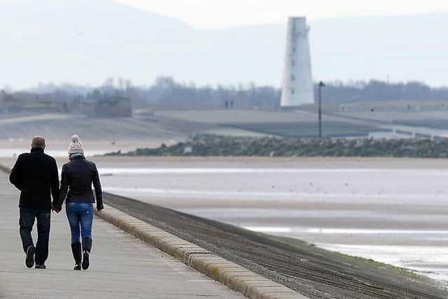 A couple walk holding hands along the seafront. (Pic credit: Paul Ellis / AFP via Getty Images)