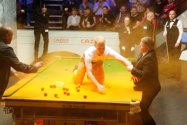 A Just Stop Oil protester is removed after jumping on the table and throwing orange powder during the match between Robert Milkins against Joe Perry during day three of the Cazoo World Snooker Championship at the Crucible Theatre, Sheffield. Picture date: Monday April 17, 2023.