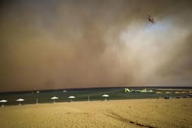A firefighting helicopter flies over a beach during a forest fire on the island of Rhodes, Greece, Saturday, July 22, 2023. PIC: Argyris Mantikos/Eurokinissi via AP