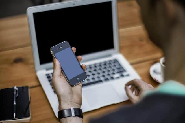 A person holding a phone at a computer.