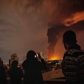 Residents look on and take pictures as flames and smoke rise from an oil storage facility struck in Tehran, Iran. PIC: Arileza Sotakbar/ISNA via AP