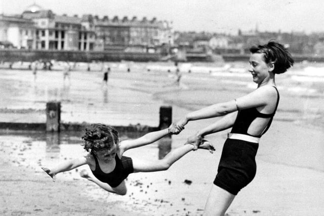 A woman swings a child on the beach at Bridlington during Whitsun holiday in June 1936.