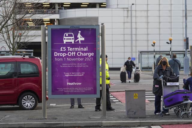 Passengers walk past an information sign at Terminal 3 of Heathrow Airport, London, advising of the new drop-off charge for people transporting travellers to the airport by vehicle. (Photo credit: Steve Parsons/PA Wire)