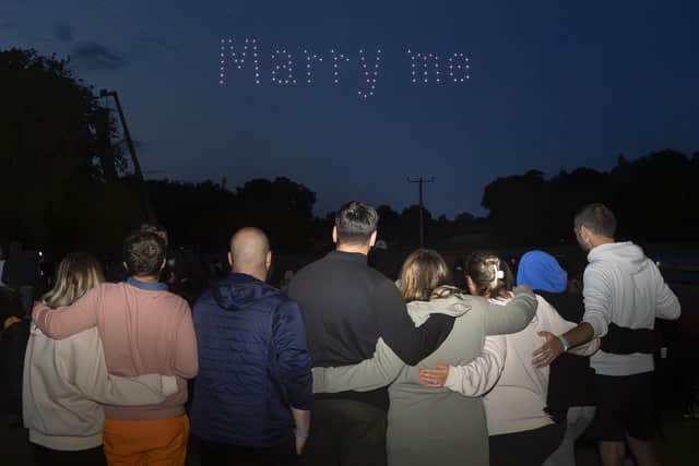 Drones spell out the words "Marry me" as Rhys Whelan (forth left) proposes to Megan Greenwood (fifth left) as they embrace with friends, during a surprise proposal at the Fireworks Championships 2023 at Newby Hall, near Ripon