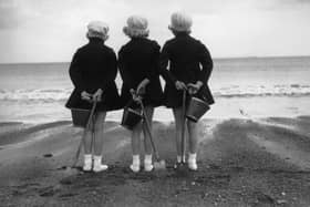 Three children wearing their coats and berets brought their buckets and spades to the beach in 1930.