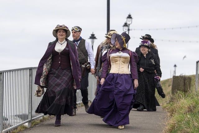 Dressed up guests walking along Whitby beach at Whitby Steampunk Weekend.
