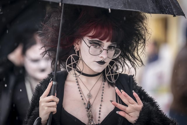 A close up of a goth enthusiast dressed up for the event and shielding from the rain.