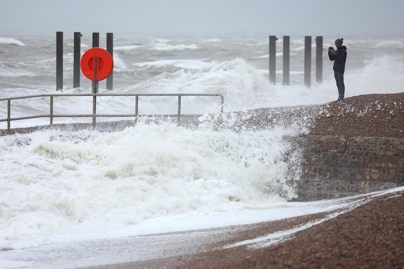 A man photographs waves from the beach at high tide, during strong winds on December 27, 2023.