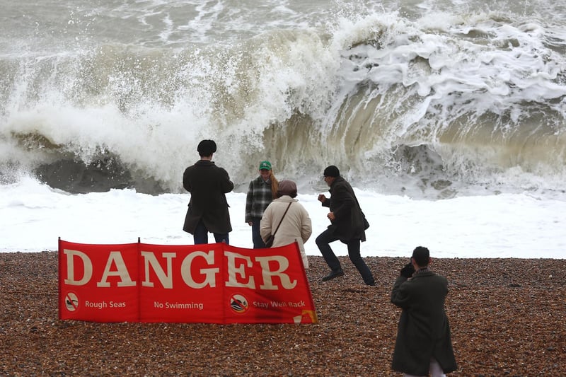 People walk on the beach at high tide, during strong winds on December 27, 2023.