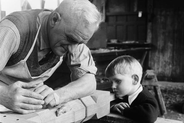 A four-year-old watches as wood carver, Reg Hunter, carves the company’s trademark mouse on the leg of a table in the Thompson’s furniture workshop in Kilburn, near Coxwold in April 1959.